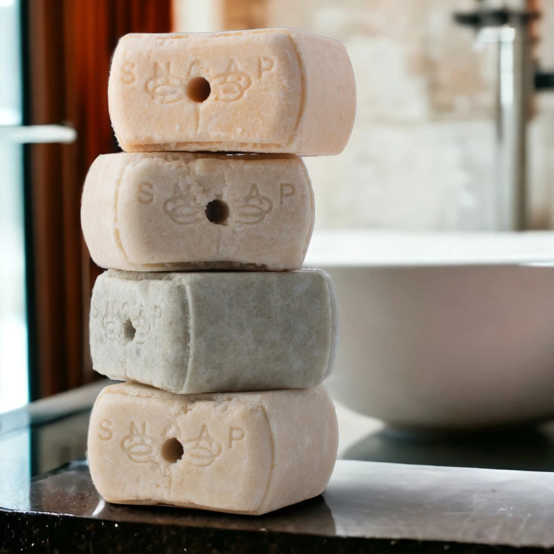 Stack of SNOAP solid shampoo and conditioner bars for refillable dispenser in bathroom setting, eco alternative to liquid haircare bottles