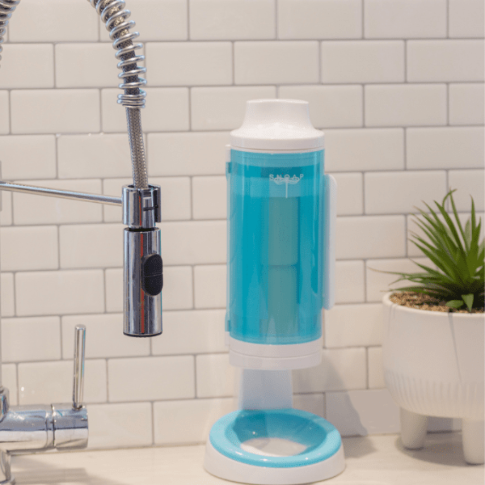 SNOAP Dispenser in white & SNOAP blue, counter mounted on white tiles with large kitchen tap.