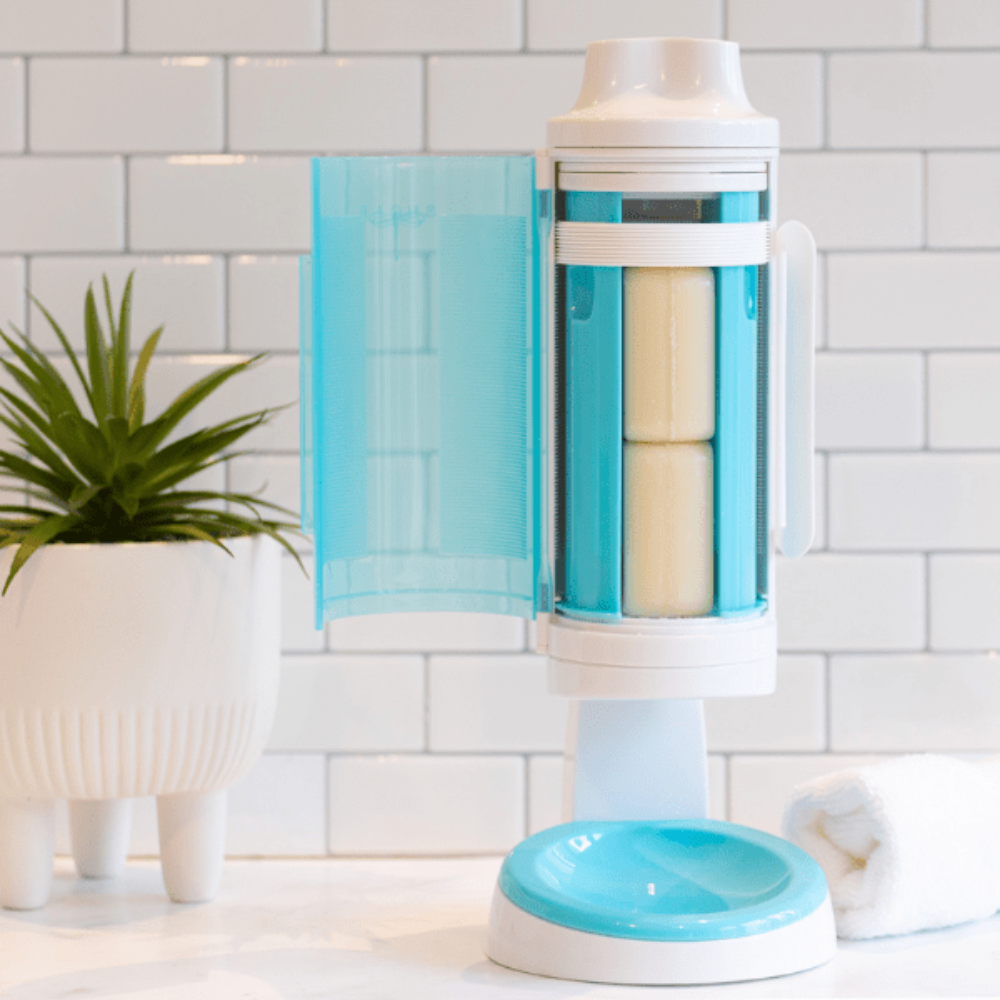 SNOAP dispenser in white and SNOAP blue on counter stand on white tiles with plant.